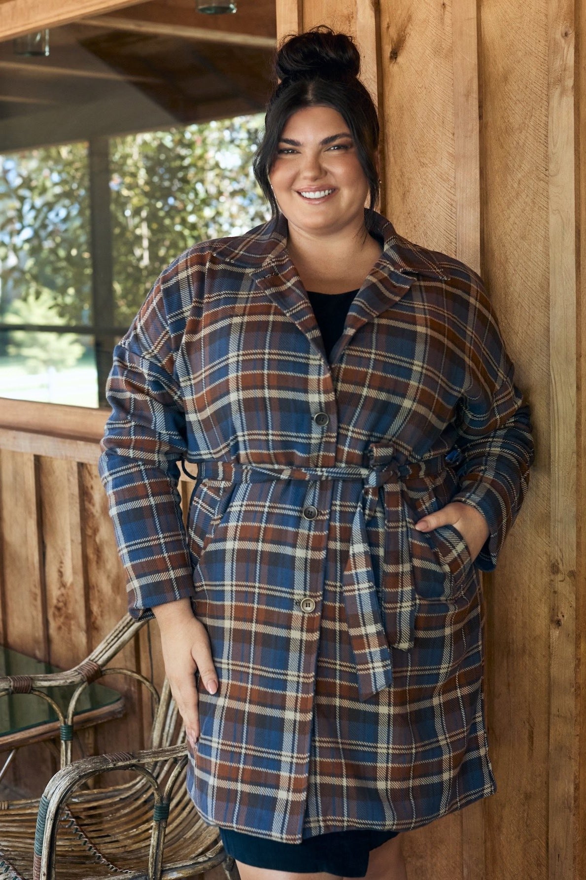 Woman wearing a flowing floral dress, standing against a backdrop of greenery.