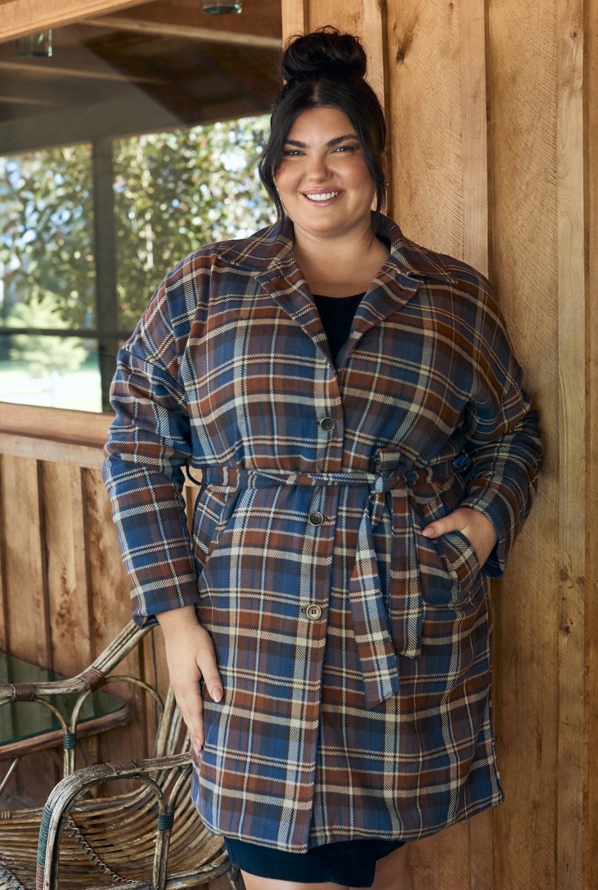 Woman wearing a flowing floral dress, standing against a backdrop of greenery.