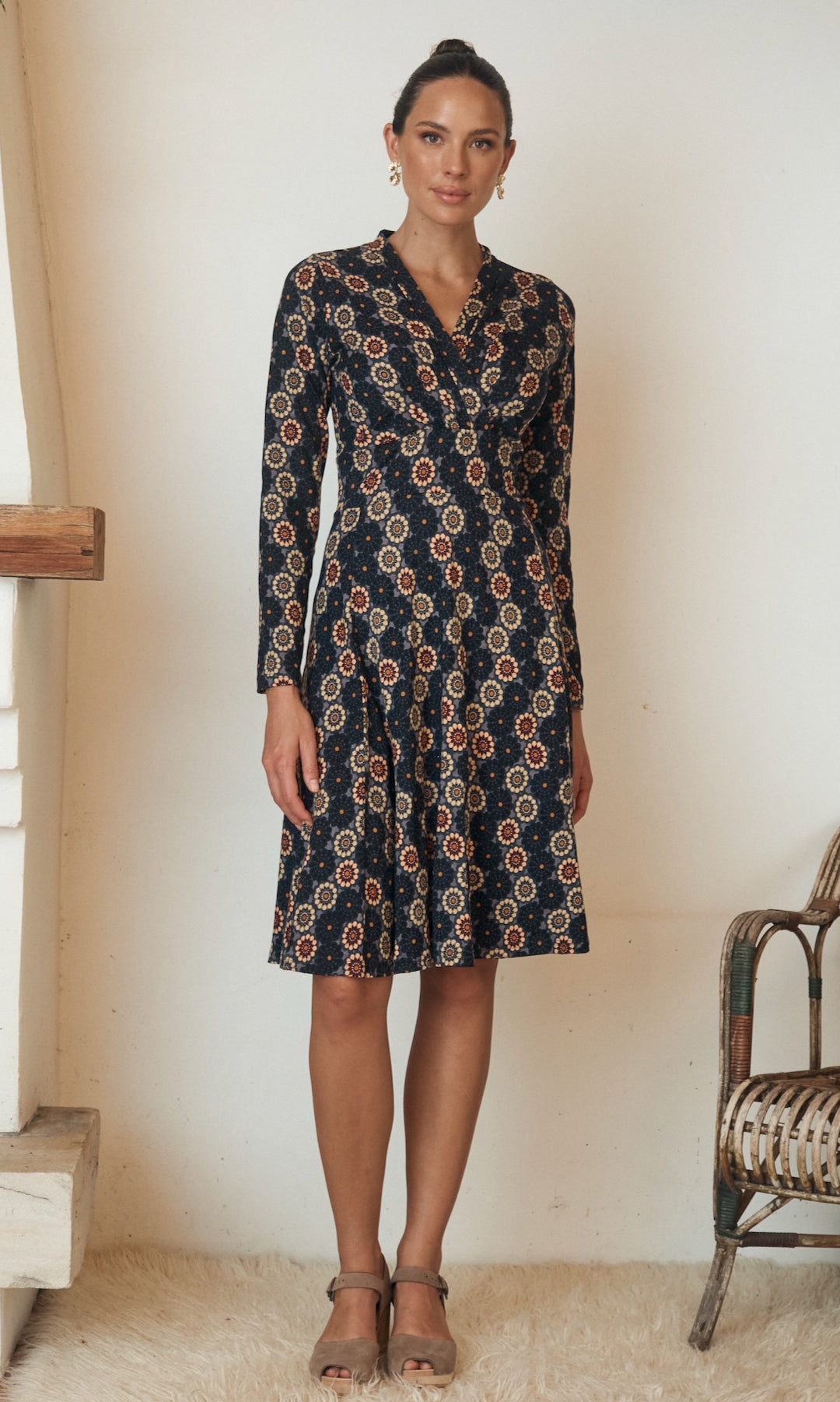 Woman posing in a long, flowy dress with floral designs and puffed sleeves.