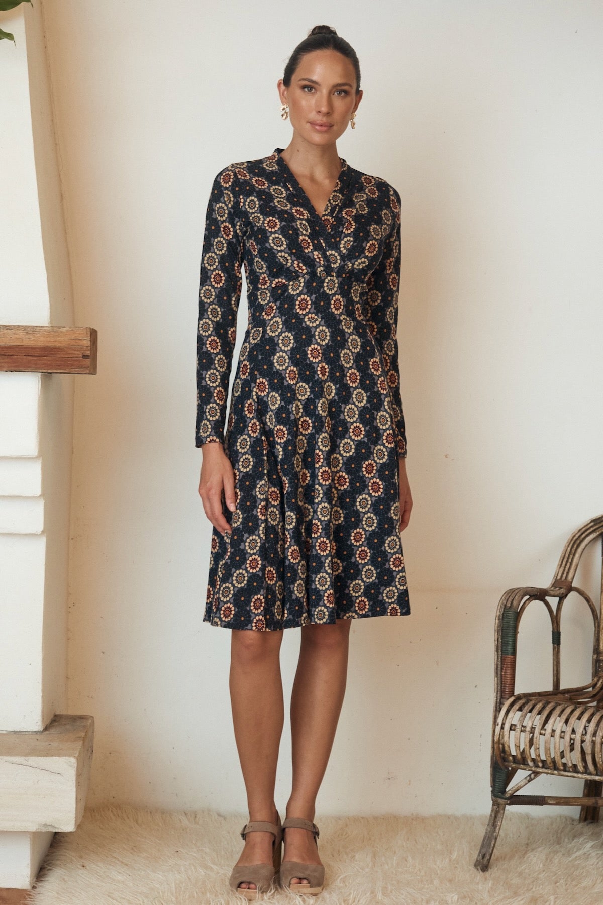 Woman posing in a long, flowy dress with floral designs and puffed sleeves.