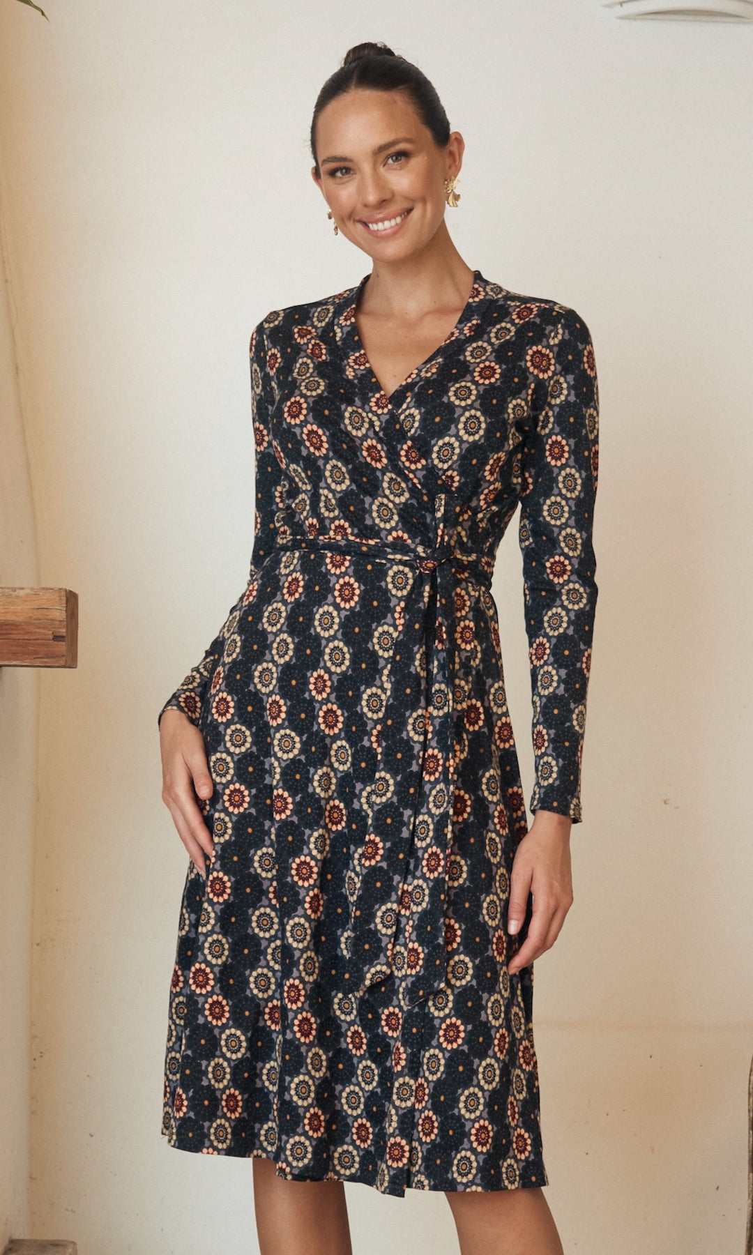 Model in a long-sleeve floral print dress, posing against a rustic background.